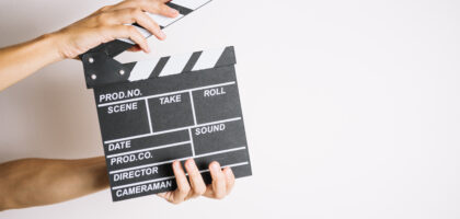 Hands holding a clapperboard against a white background with unfilled text fields for production details, illustrating the preparation for adding elements like French subtitles to a film or TV show.